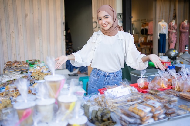 Fille asiatique souriante en hijab avec des gestes de la main offrant une variété d'aliments frits par décrochage