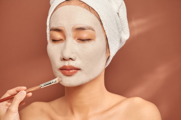 Fille asiatique de spa appliquant le masque facial d'argile. Soins de beauté. Sur fond bleu.