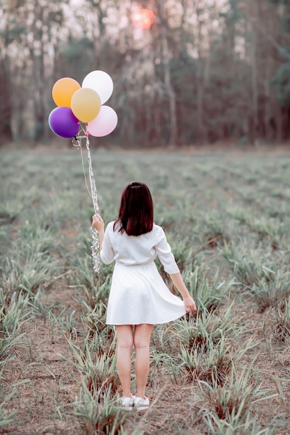 Fille asiatique tenant des ballons dans un champ.