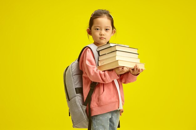 fille asiatique tenant garde beaucoup de livres et ont un sac à dos sur les épaules debout jaune isolé