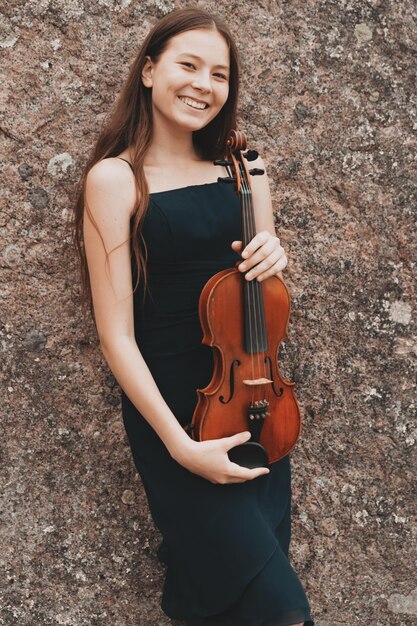 Fille asiatique avec un violon sur le fond d'un mur de pierre