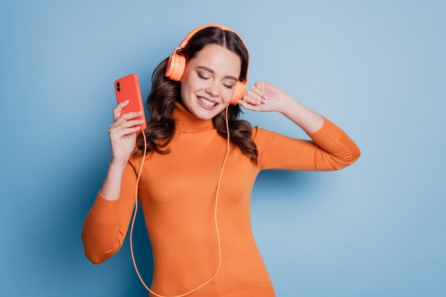 Fille assez cool écoutant de la musique dans les écouteurs tenir le téléphone fermer les yeux danser sur fond bleu