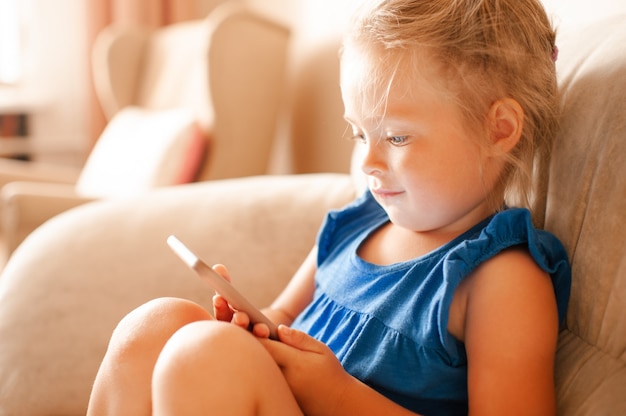 Fille assez mignonne d'enfant tenant le téléphone intelligent regardant des dessins animés