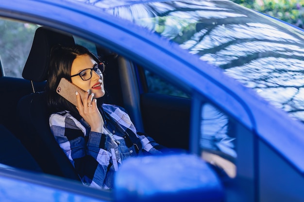 Fille assise au volant d&#39;une voiture et parlant par téléphone