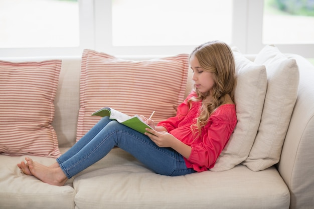 Fille assise sur le canapé et faire ses devoirs dans le salon