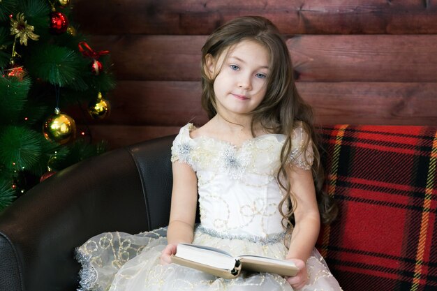 Fille assise sur un canapé avec un livre dans ses mains.