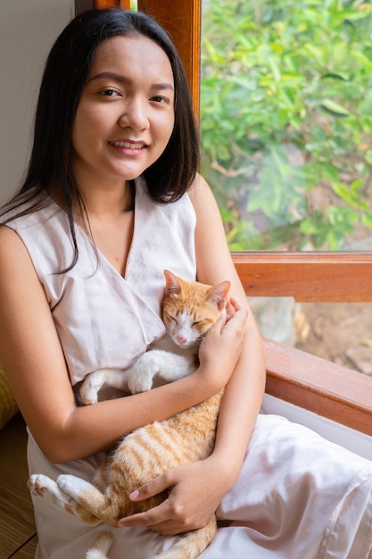 La fille assise avec un chat à la fenêtre à la maison