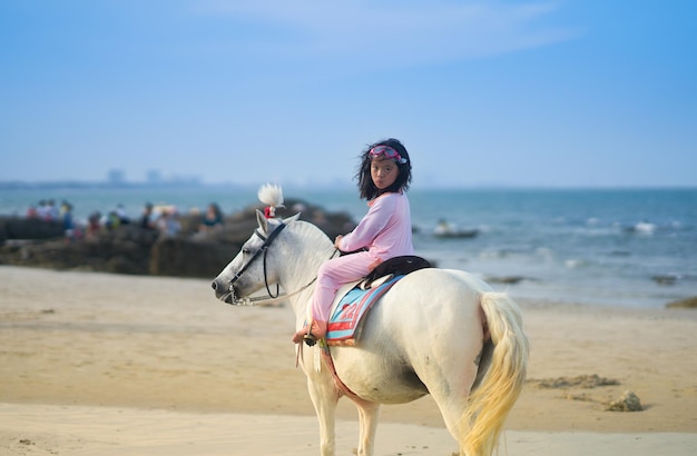Une fille assise à cheval sur la plage contre le ciel.