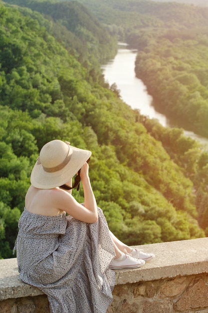 Fille assise sur une colline et prend des photos dans le contexte d'une forêt