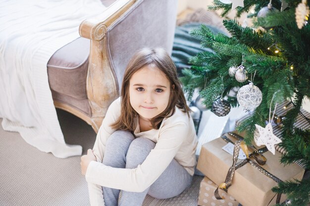 Fille assise à côté de l'arbre de Noël à la maison