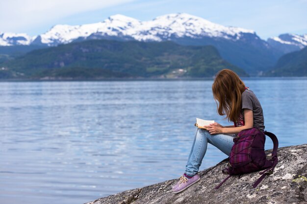 Fille assise sur une côte de fjord et lisant