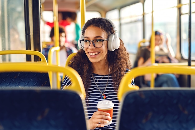 Photo fille assise dans un bus, boire du café, écouter de la musique et regarder la fenêtre de l'auge.