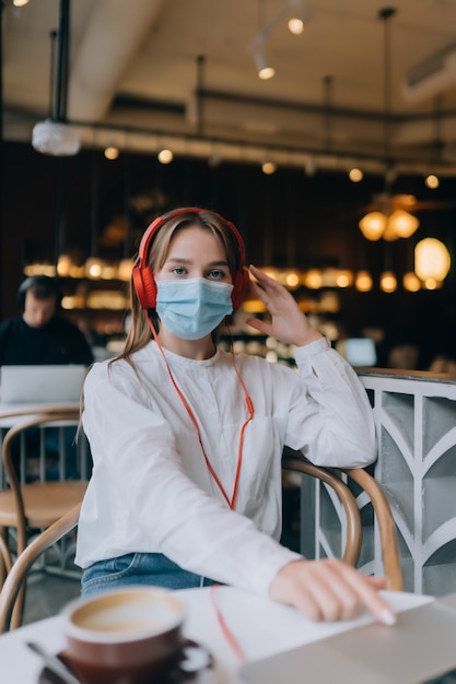 Une fille assise dans un café avec des écouteurs épidémie de coronavirus