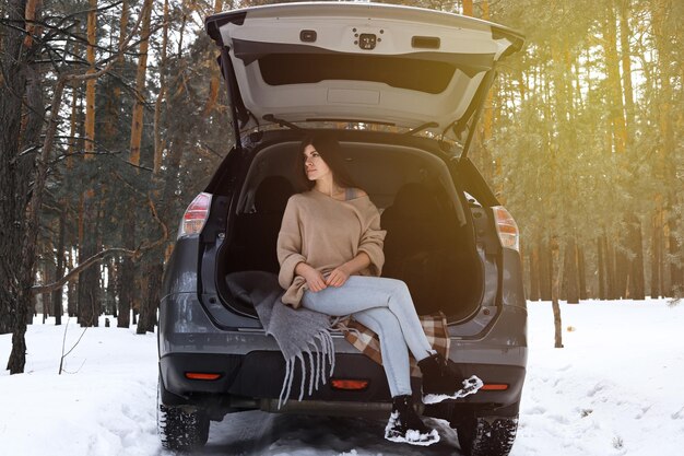 Fille assise dans le coffre d'une voiture dans la forêt d'hiver profitant d'un voyage