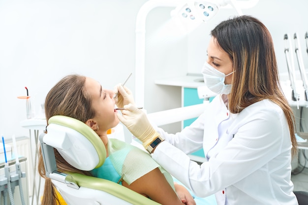 Fille assise sur un fauteuil dentaire avec la bouche ouverte pendant l'examen oral pendant que le médecin. Visite chez le dentiste. Concept de dentisterie.