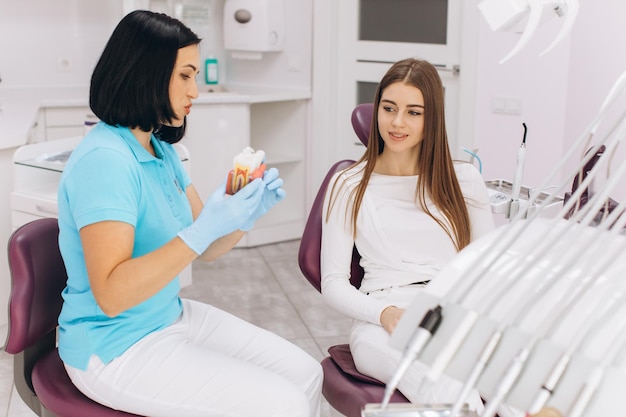 Fille assise sur un fauteuil dentaire lors d'une visite chez la femme dentiste montrant une carie sur le modèle