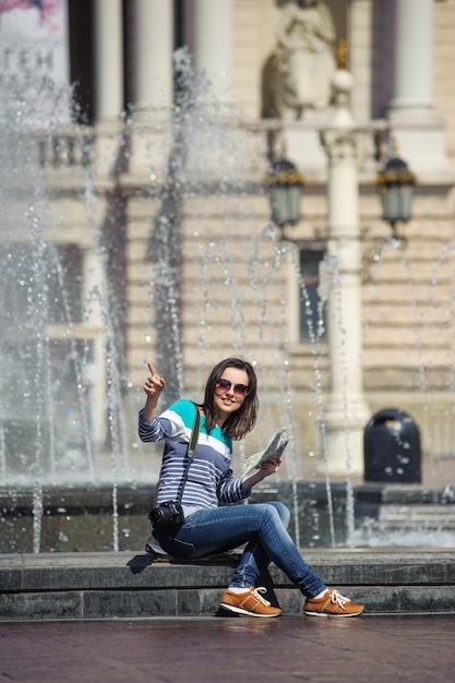 Fille assise à la fontaine avec carte et caméra montrant le chemin