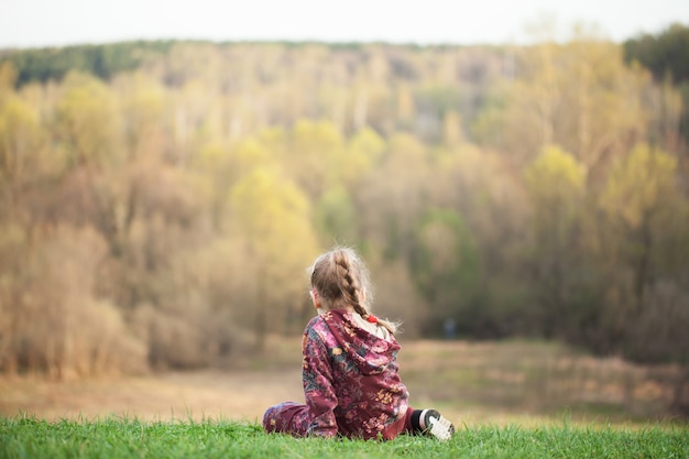 Fille assise sur l'herbe sur le fond des arbres. grande colline verte