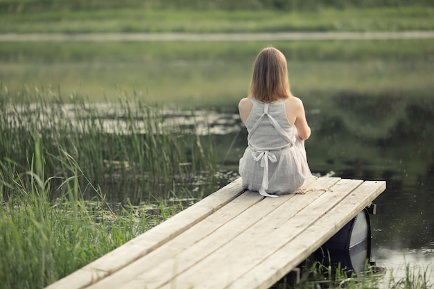 fille assise sur la jetée au bord du lac et rêve de la vie