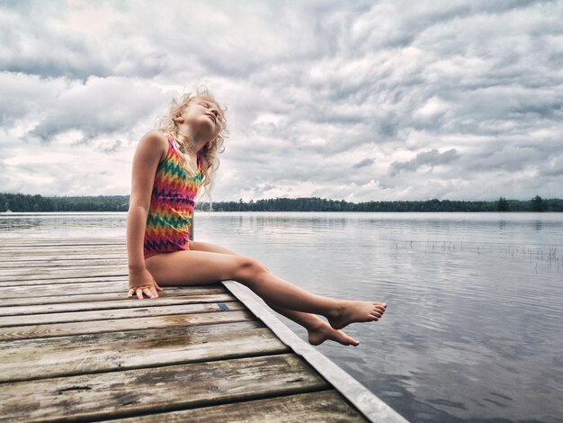 Une fille assise sur une jetée au-dessus d'un lac contre le ciel