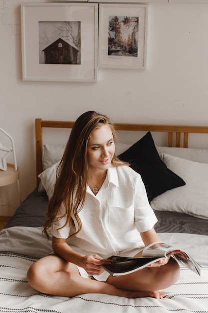 Fille assise sur le lit et feuilletant un magazine