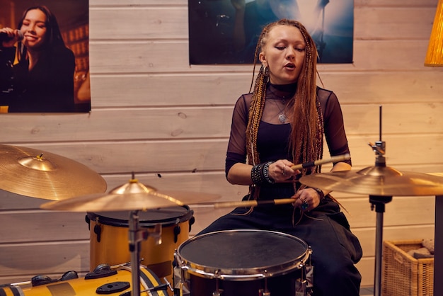 Fille assise par batterie tout en enregistrant de la musique dans un studio moderne