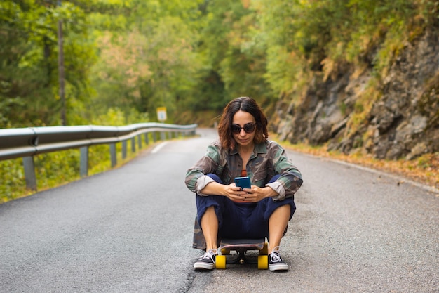 Fille assise sur une planche à roulettes à l'aide de son téléphone