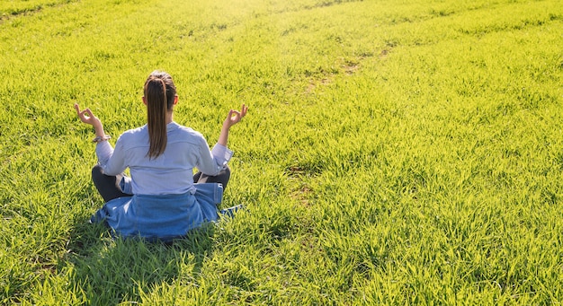 Fille assise sur un pré vert au printemps avec la méditation pose sur une journée très ensoleillée