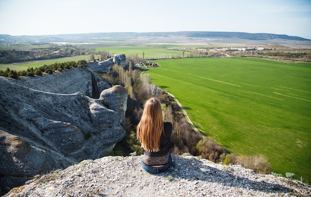 Fille assise sur un rocher sur un champ vert