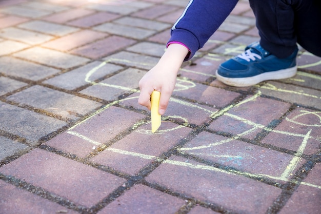 Fille assise sur une route asphaltée en béton., Sur un chemin en pierre. enfants peignant des lignes, des nombres à la craie sur l'asphalte. mise au point sélective.Petite fille mains peignant sur le trottoir à l'aide d'une craie colorée.