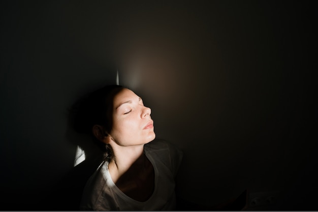 Fille Assise Seule Dans La Poche Du Soleil Dans Une Pièce Sombre. Concept De Santé Mentale