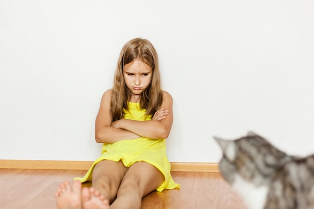 Fille assise sur le sol, bouleversée, offensée par le chat, animal de compagnie, rayé, main, pieds, robe jaune, bébé, famille, soins aux animaux