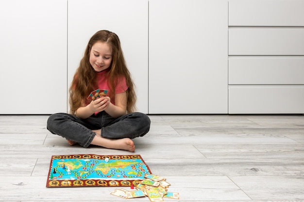 Une fille assise sur le sol à la maison tient des cartes à jouer dans ses mains un jeu de société est disposé sur le sol