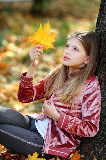 Fille assise sous l'arbre dans le parc d'automne