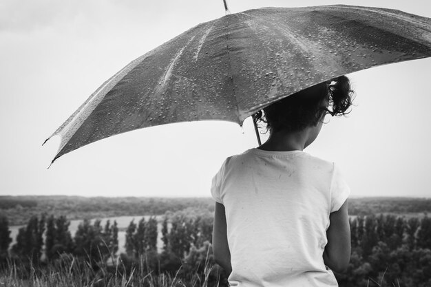 Fille assise sous la pluie battante avec un parapluie