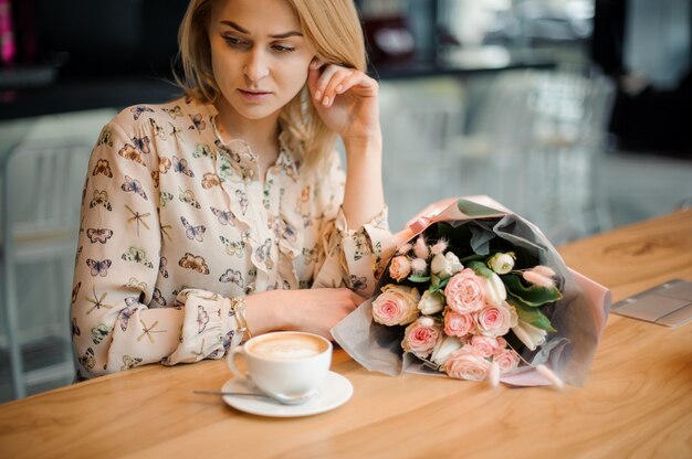 Fille assise à la table avec une tasse de café et un beau bouquet