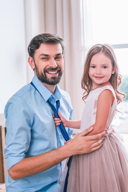 Fille attachant une cravate à son père et souriant à la caméra dans le salon