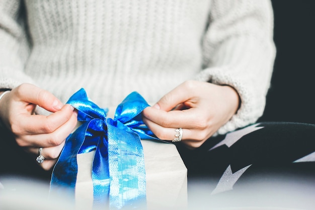 La fille attache un arc sur un cadeau. Emballage cadeau. Cadeau avec un arc bleu. Cadeau en papier kraft