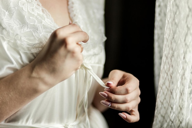 Fille attache la ceinture sur sa robe debout près de windowwoman se prépare avant la cérémonie de mariage