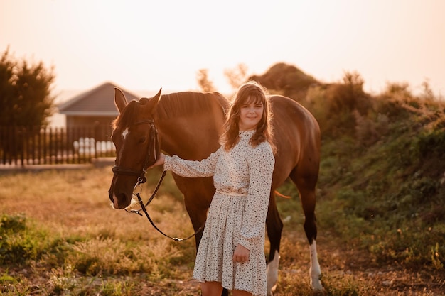 Une fille atteinte de paralysie cérébrale vêtue d'une robe légère et d'un chapeau blanc se moque d'un cheval brun