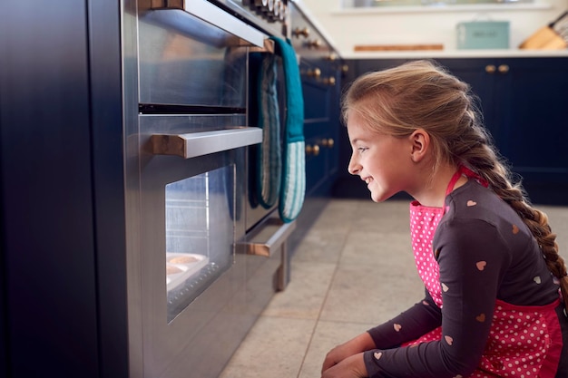 Fille en attente par four dans la cuisine à la maison pour les gâteaux à cuire