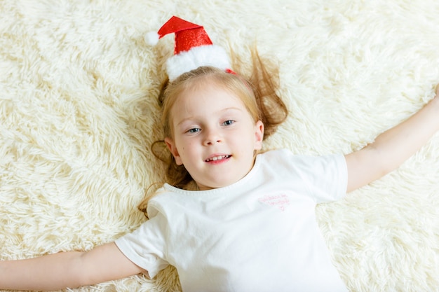 Fille au bonnet rouge est allongée sur une couverture blanche.