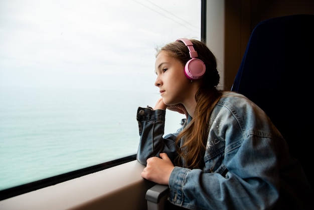 Une fille au casque dans un train regarde par la fenêtre. Périple.