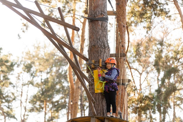 La fille au casque orange dans le parc d'aventure s'accroche aux cordes