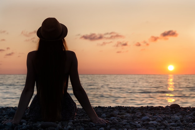 Fille au chapeau assis au bord de la mer