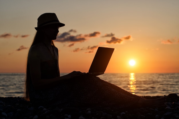Photo fille au chapeau assis et travaillant sur son ordinateur portable
