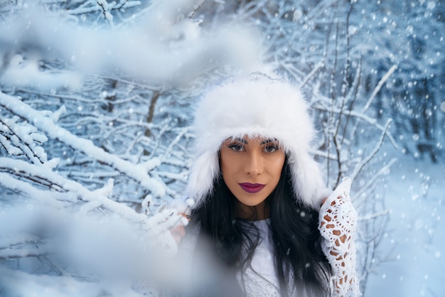 Fille au chapeau blanc posant entre les branches des arbres enneigés.