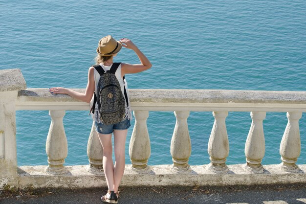 Fille au chapeau debout dans les escaliers et regardant la mer. Vue de l'arrière