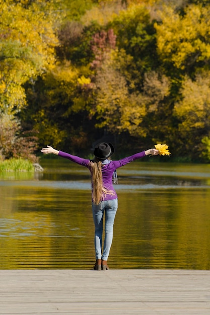 Fille au chapeau debout sur la jetée à bras ouverts Journée ensoleillée d'automne Vue arrière