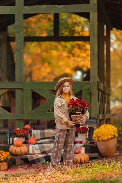 Fille au chapeau avec un décor d'automne avec des citrouilles et des fleurs